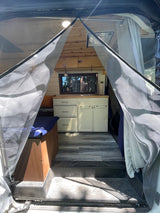 RV rental interior: A cozy camper van with a kitchenette, bench, wood ceiling, and bug screen at the entrance.