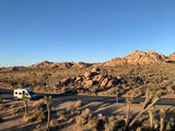 White rv rental on a road in Joshua Tree National Park. Desert landscape with unique flora and rock formations.