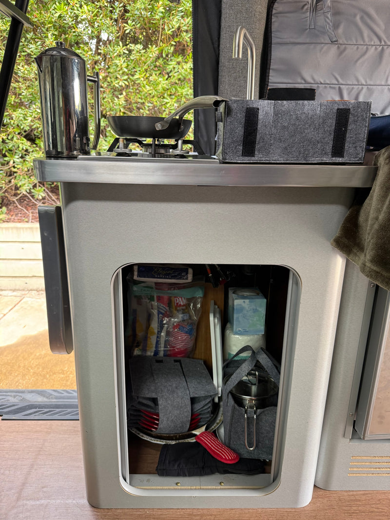 Inside an rv rental, a compact kitchen features a stove, sink, coffee maker, and open storage with supplies and cookware. — photo 20