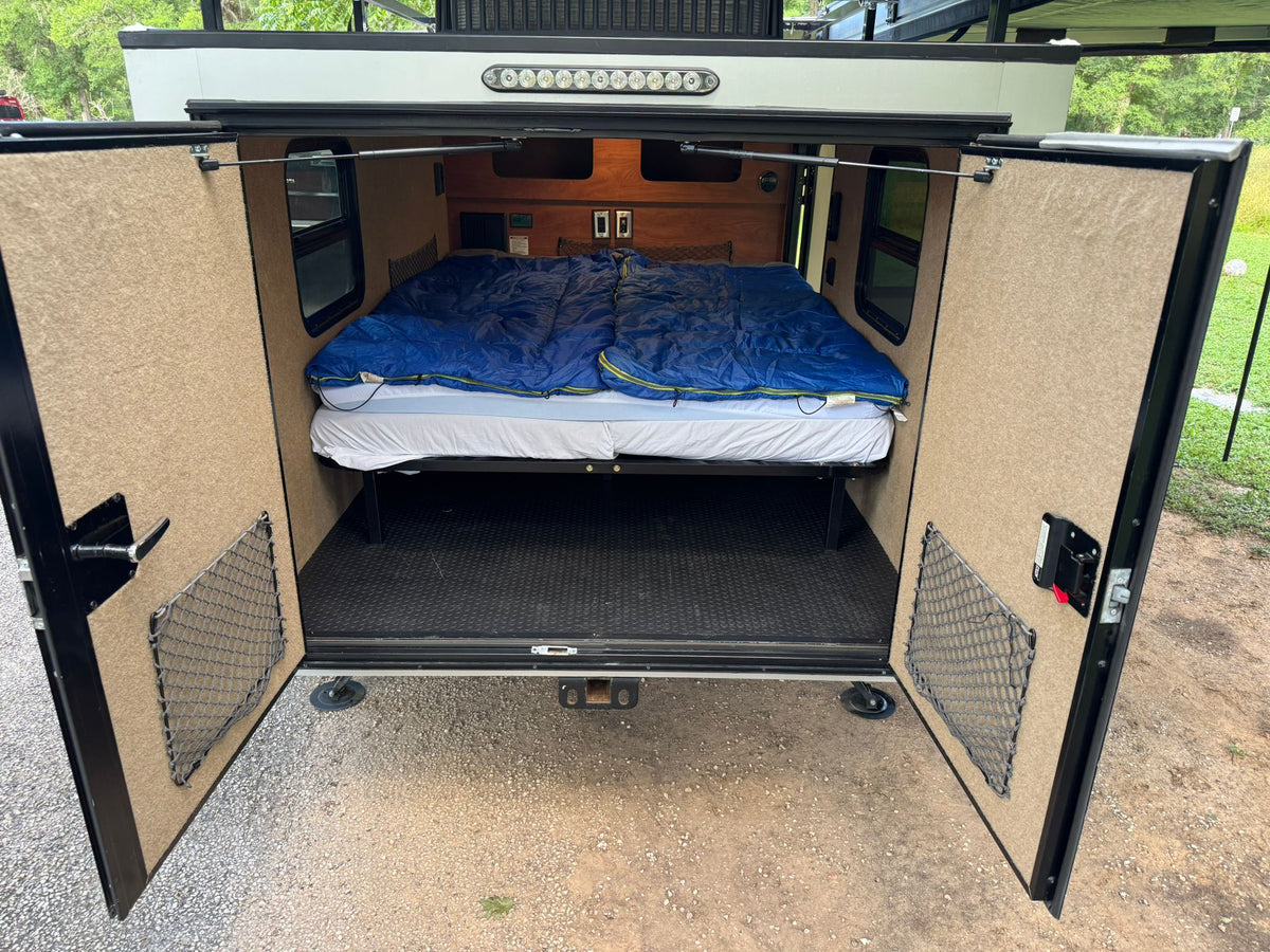 RV rental's rear hatch open: reveals a cozy queen bed, wood paneling, and door storage inside this camper. — photo 4