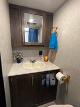 Compact RV rental bathroom with vanity, sink, mirrored cabinet, towel, and storage, perfect for travel.