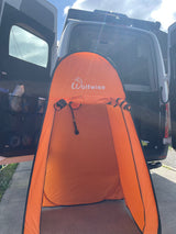 Orange Wolfwise pop-up privacy tent with shower inside, set up behind an RV rental van for convenient camping.