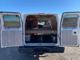 An RV rental camper van conversion reveals its rear interior with a raised bed platform and organized storage below.