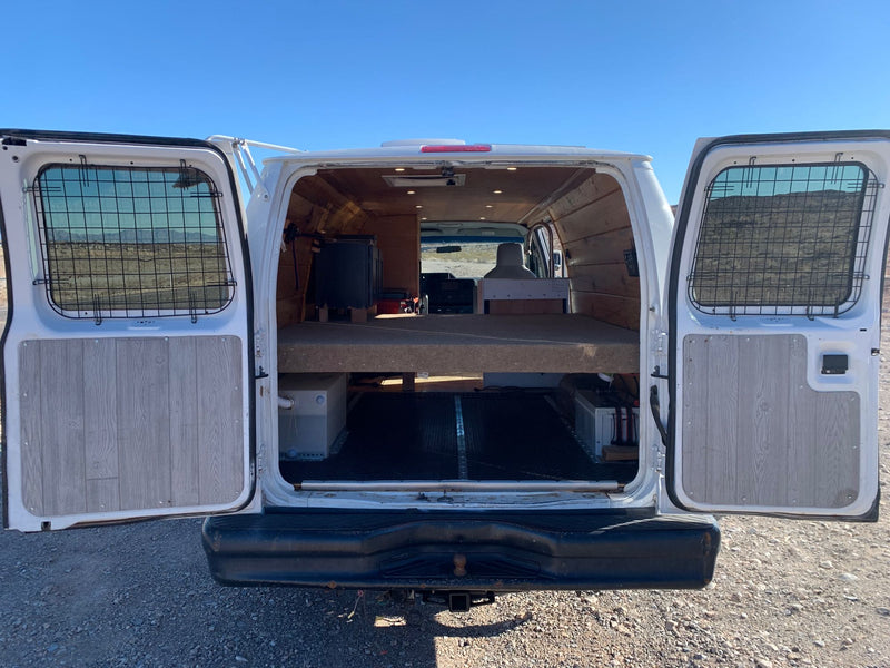 under a clear blue sky. Scenic desert travel.|Off-grid RV rental van with solar panels parked in a rugged Nevada desert landscape near mountains under a clear blue sky.|An RV rental camper van conversion reveals its rear interior with a raised bed platform and organized storage below.|RV rental conversion van: Open side door reveals a compact kitchen with sink — photo 4