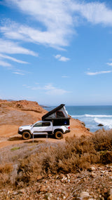 Coastal camping: White pickup truck with deployed pop-up camper on a cliff overlooking the ocean. RV rental ready!