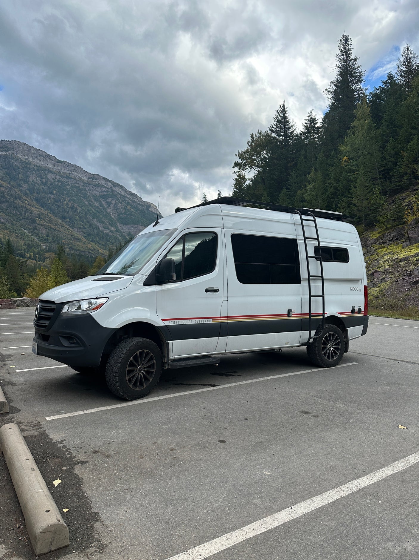 White Mercedes Sprinter rv rental van parked in a mountain lot under cloudy skies, ready for overland adventures.