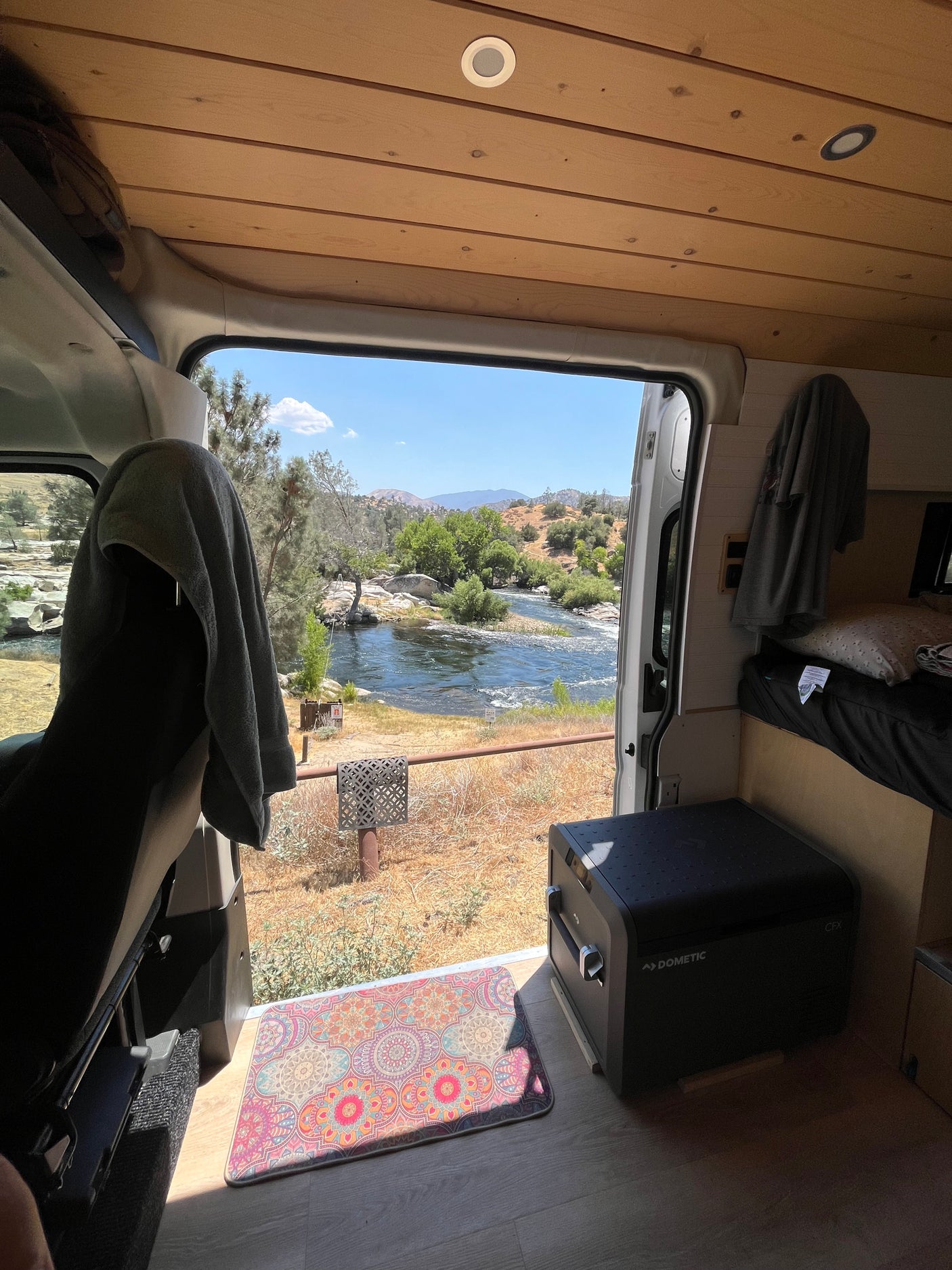 RV rental van interior: a cozy setup overlooking a beautiful river and distant mountains. Dometic fridge.