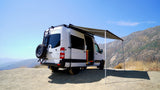 White camper van with awning deployed on a mountain road. Perfect for your next RV rental adventure.