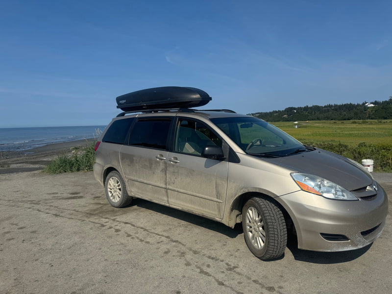  offering a journey like a compact rv rental.|Road trip ready: Toyota Sienna minivan with Yakima cargo box by the ocean. Consider this for your next rv rental adventure!|This gold minivan RV rental with a roof box is parked by a serene ocean under a clear blue sky — photo 5