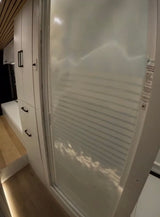 Modern RV rental interior with white storage cabinets, wood flooring, and a space-saving, frosted shower door.