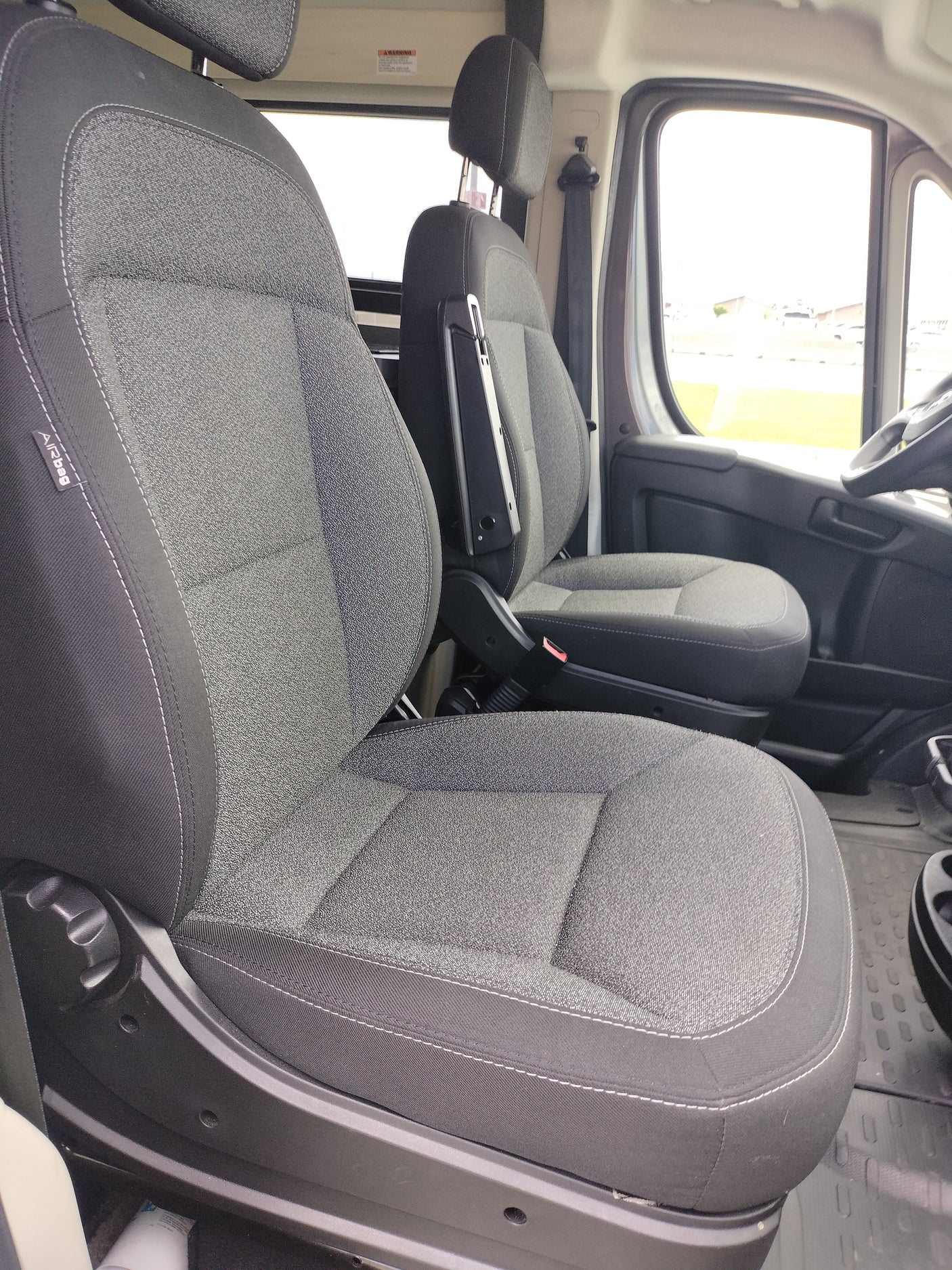 Interior of an RV rental: spacious cabin featuring comfy gray passenger and driver seats with armrests, and large windows.