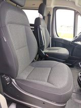 Interior of an RV rental: spacious cabin featuring comfy gray passenger and driver seats with armrests, and large windows.