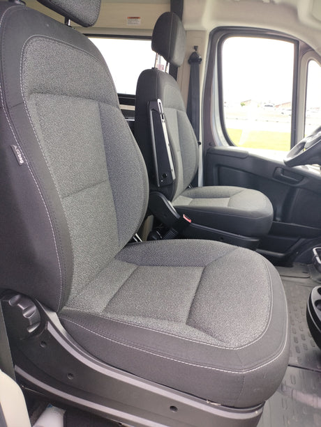 Interior of an RV rental: spacious cabin featuring comfy gray passenger and driver seats with armrests, and large windows.
