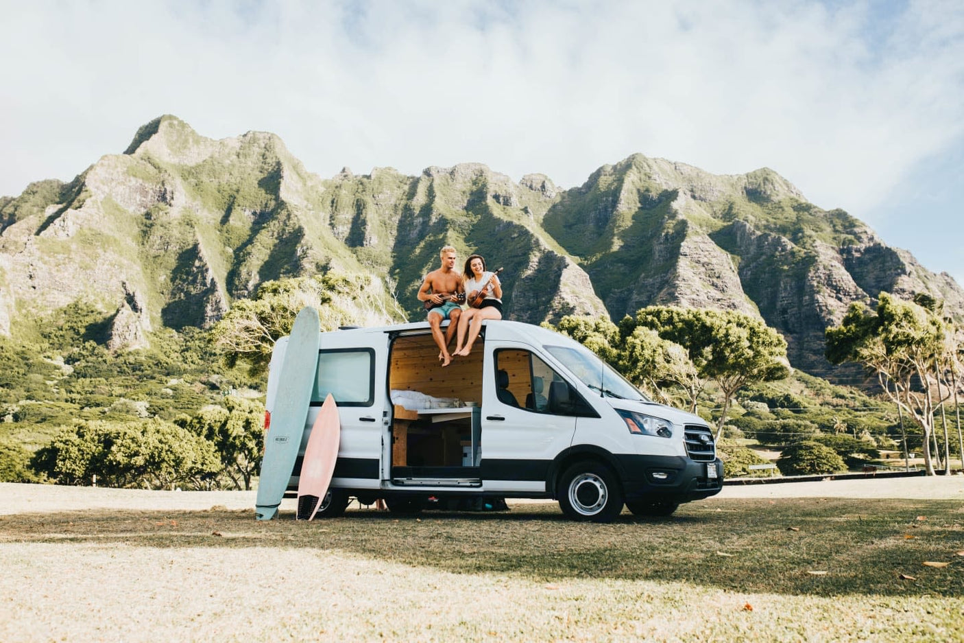 Scenic rv rental: A couple plays ukulele on their camper van roof, with surfboards & mountains.