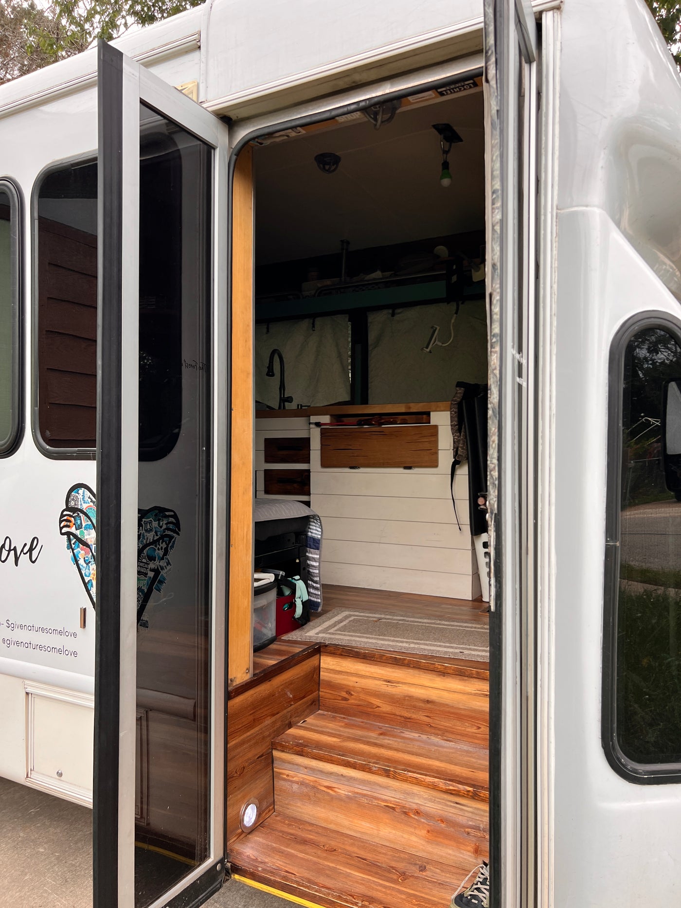 Inside a unique RV rental: custom wood steps lead to a cozy kitchen & living area in this bus conversion. — photo 11