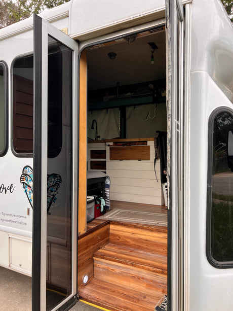 Inside a unique RV rental: custom wood steps lead to a cozy kitchen & living area in this bus conversion.