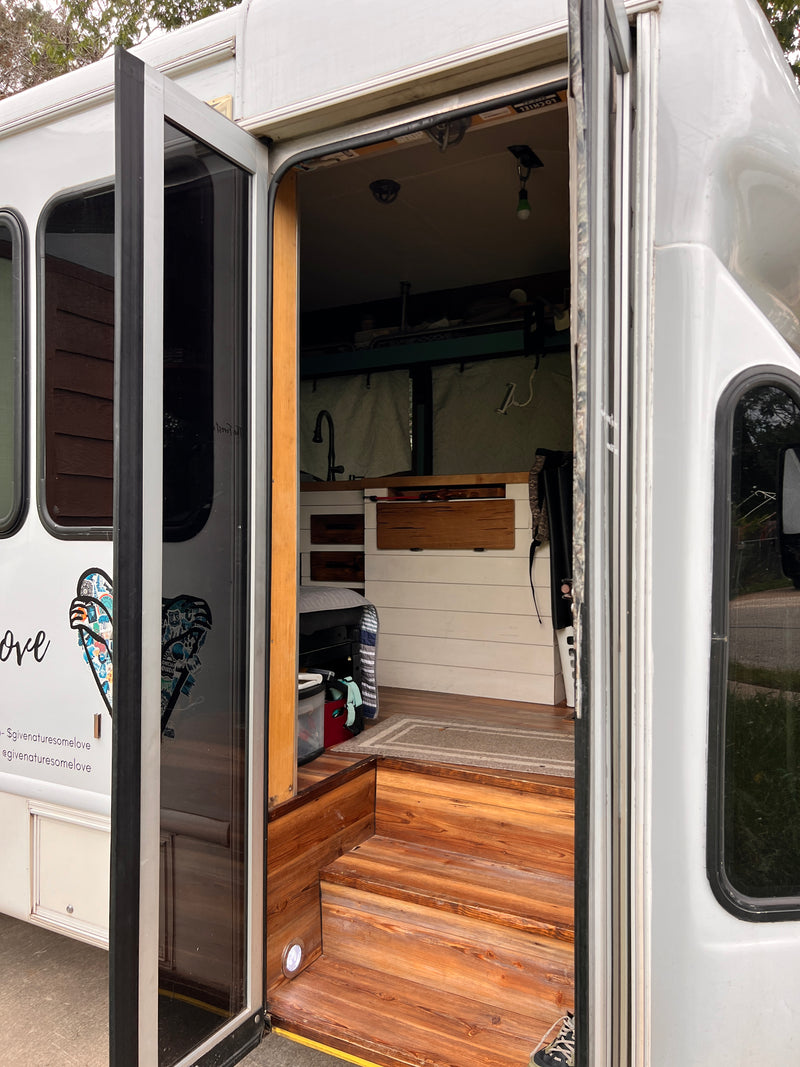 Inside a unique RV rental: custom wood steps lead to a cozy kitchen & living area in this bus conversion. — photo 11