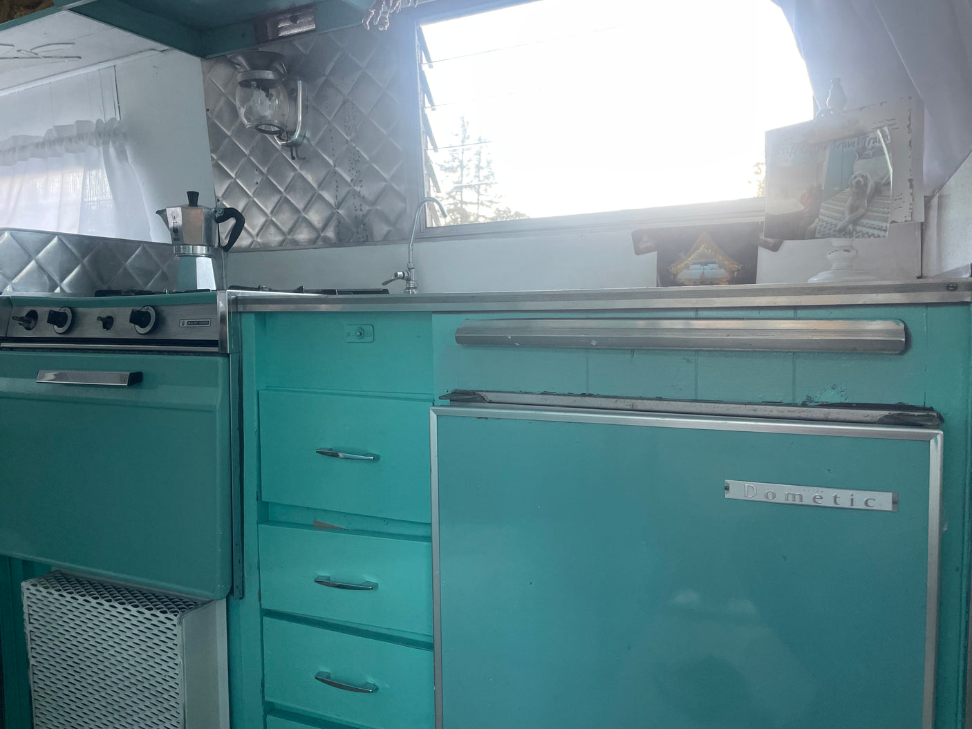This RV rental features a vintage teal kitchen with a Magic Chef stove, Dometic fridge, and a moka pot.