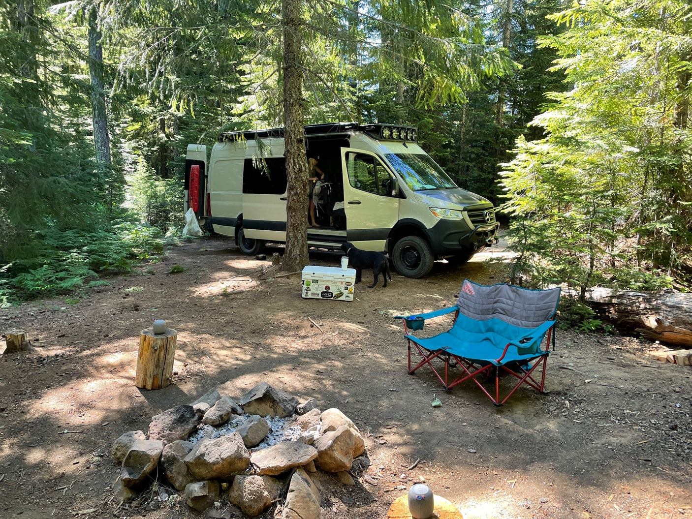 Enjoying a tranquil forest camp. This RV rental offers off-grid comfort with a fire pit, cooler, and dog in nature's embrace.