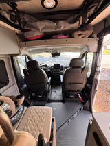 View inside an RV rental looking forward, highlighting the cockpit, two front seats, a child car seat, and overhead storage compartments.