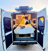 Open rear doors of an RV rental camper van reveal a comfortable bed and mosquito net inside, ready for adventure at sunset.