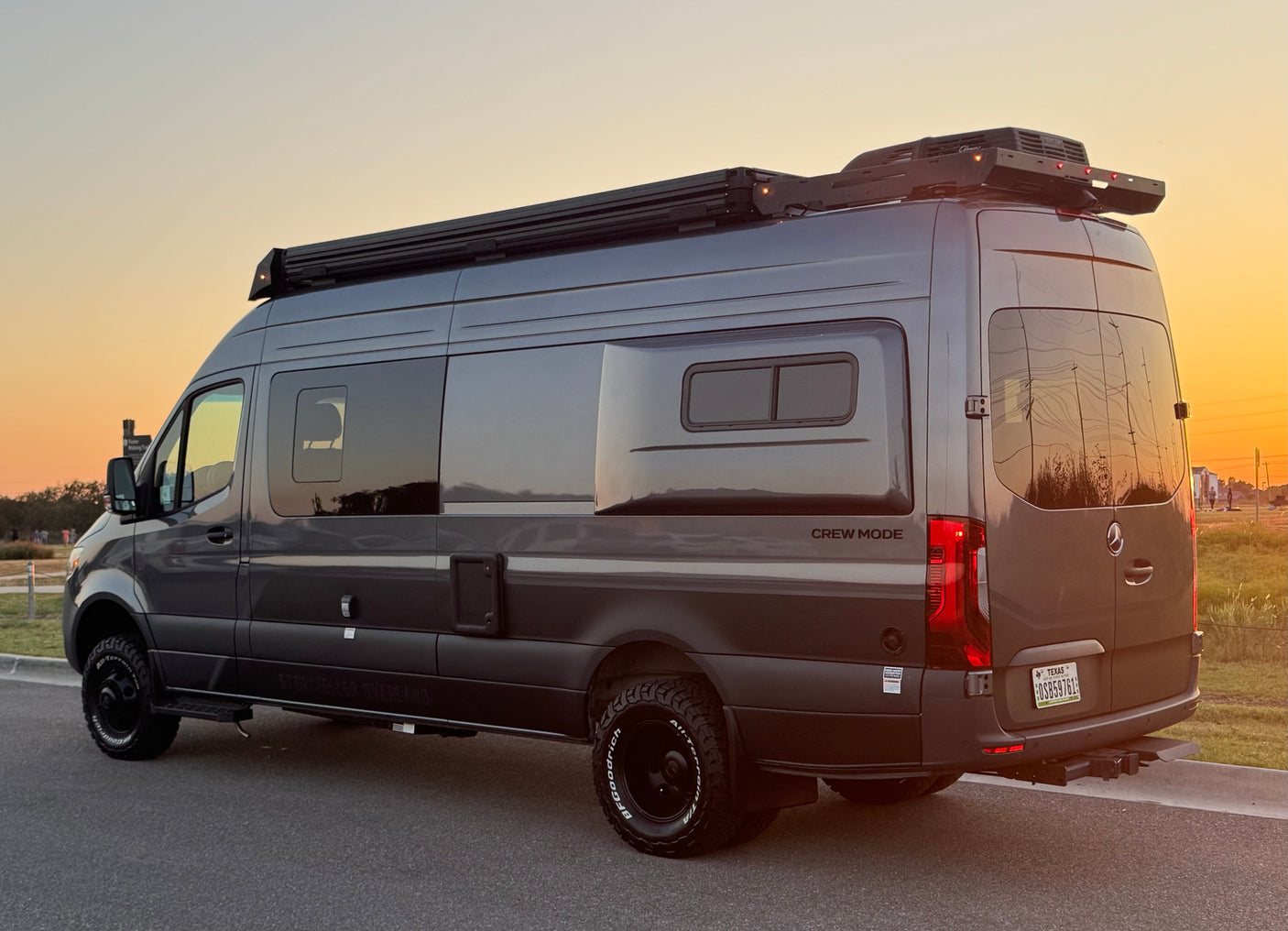 Gray Mercedes Sprinter camper van, ideal for rv rental adventures. Features roof rack, off-road tires, seen at sunset.
