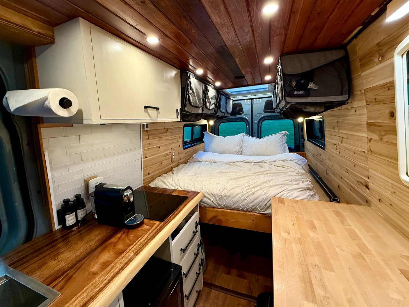 Explore this charming rv rental! A custom van interior with a bed, kitchen, and overhead storage for comfy travel.