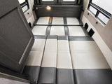 Spacious RV rental interior featuring a comfortable convertible bed with two-tone grey and off-white cushions, ideal for travel.