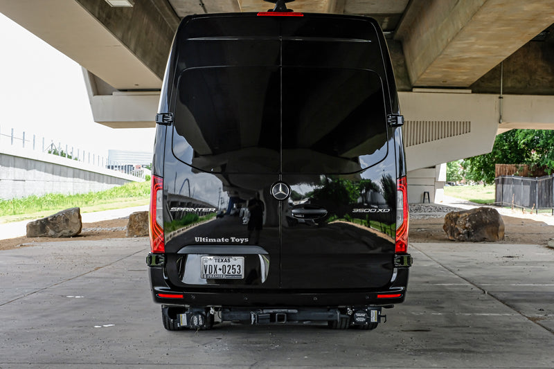 Rear view of a black Mercedes Sprinter van, a luxury camper or rv rental, parked under a bridge. "Ultimate Toys" badging visible. — photo 9