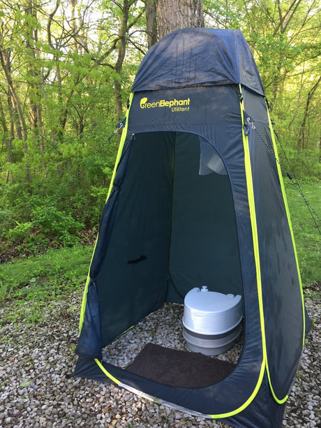 GreenElephant privacy tent with portable toilet on gravel, surrounded by trees. Ideal for your RV rental adventures.