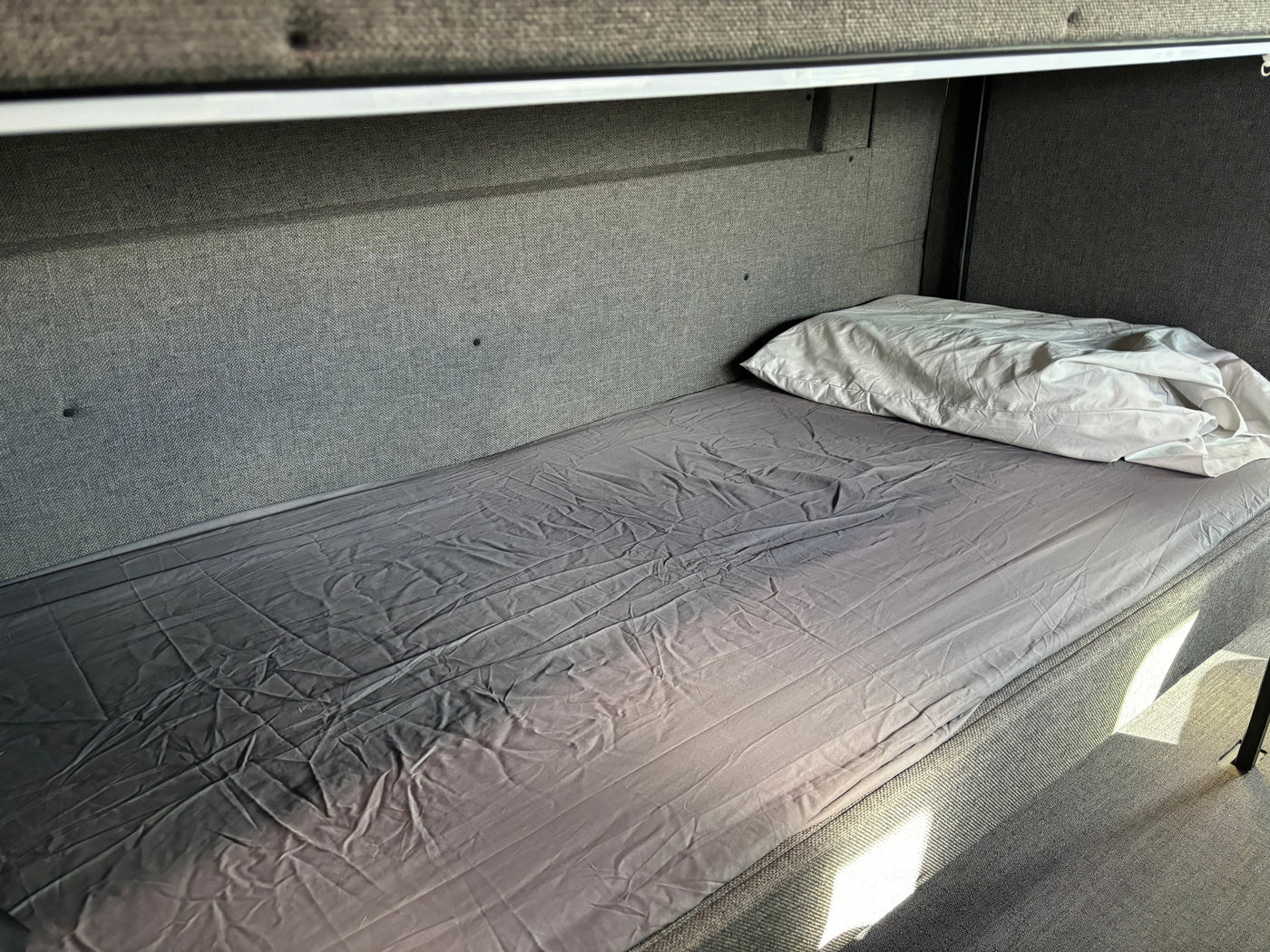 Bunk bed inside an rv rental, featuring grey fabric walls, a fitted sheet, and a white pillow for comfortable rest. — photo 8