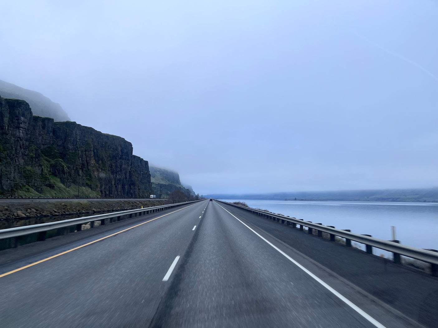 A scenic highway stretching into a misty distance, flanked by towering cliffs and a wide river. Ideal for an RV rental adventure.