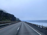 A scenic highway stretching into a misty distance, flanked by towering cliffs and a wide river. Ideal for an RV rental adventure.