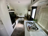 Bright RV rental interior showing a compact kitchen with stove, dinette, fridge, and sleeping loft.