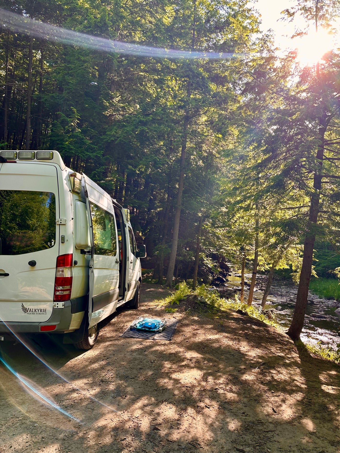 Explore nature with this Valkyrie RV rental, parked by a sun-dappled forest river. Ideal for scenic camping adventures.