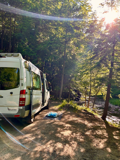 Explore nature with this Valkyrie RV rental, parked by a sun-dappled forest river. Ideal for scenic camping adventures.