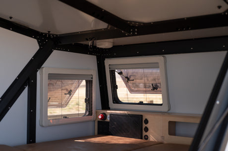Interior of an RV rental: well-appointed space with large windows, power hub, and comfy sleeping area.