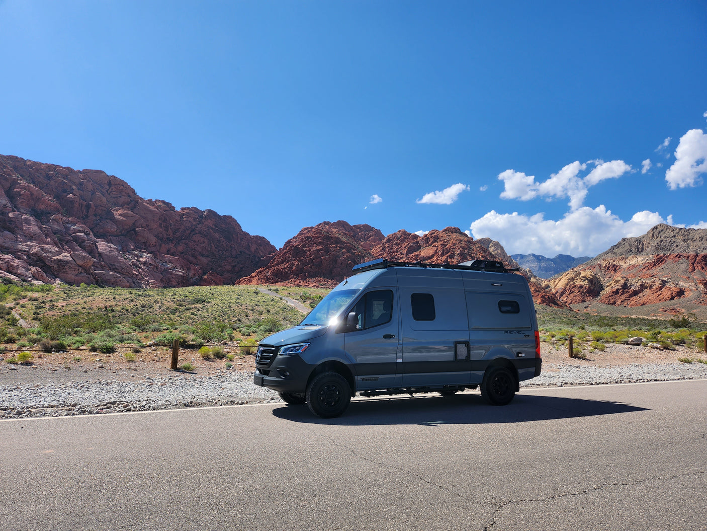 Winnebago Revel RV rental parked on a desert road, stunning red rock mountains and blue sky in the background. Perfect for adventure!