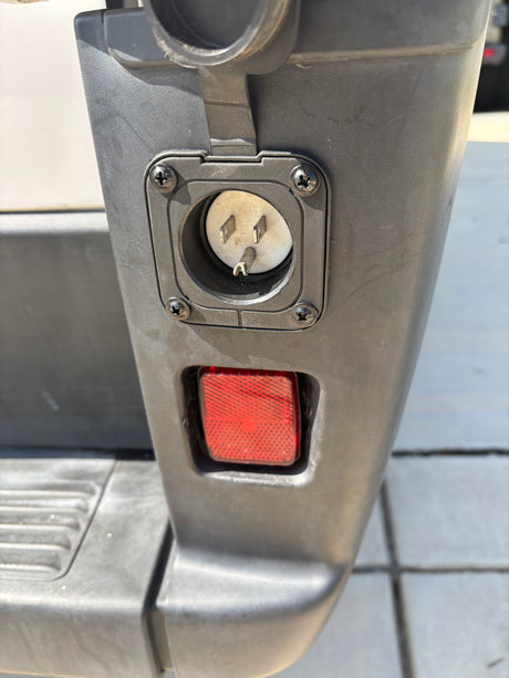 Exterior of an RV rental, featuring its shore power inlet (a 3-prong electrical connection) and a red reflector below.