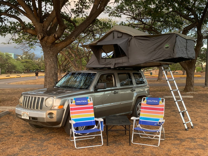Gray Jeep Patriot SUV with open rooftop tent, ladder, colorful chairs & table. Compact rv rental for camping. — photo 4