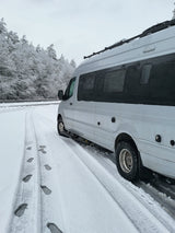 White RV rental on a snowy road with frosted trees and footprints visible in winter.