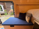 Cozy rv rental interior with wooden walls, a blue cushioned bench/bed, and pillows, offering an outdoor view.