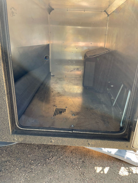 View inside an RV rental's metallic storage compartment. Mostly empty, with a mat and small items, showing use.