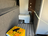 RV rental's utility storage shows a water tank, a flexible hose, and yellow CAMCO leveling blocks on a patterned floor.