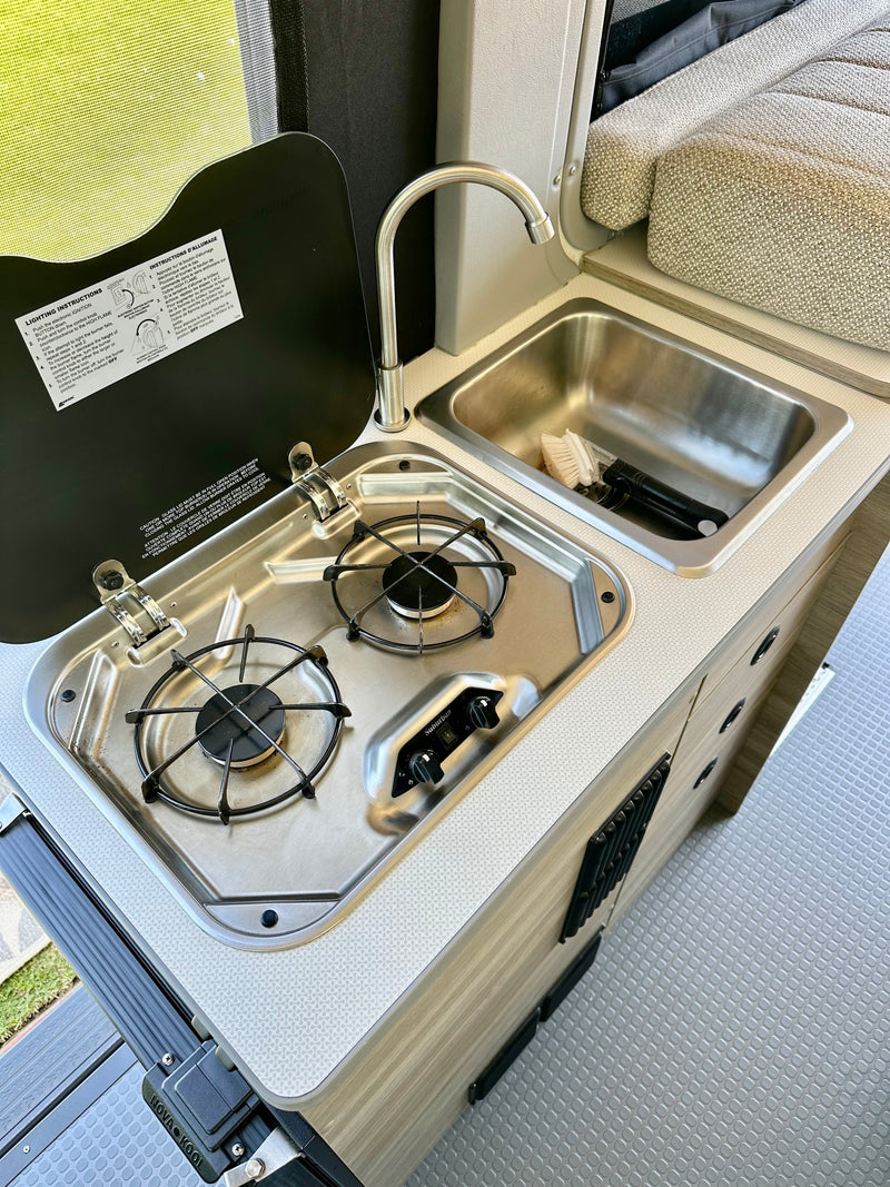 Compact RV rental galley: two-burner stove, sink, faucet, and a tidy counter area for cooking on the go. — photo 9