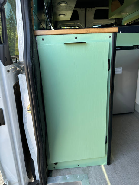 This RV rental interior features a mint green custom cabinet, wood countertop, and refrigerator, ideal for van life.