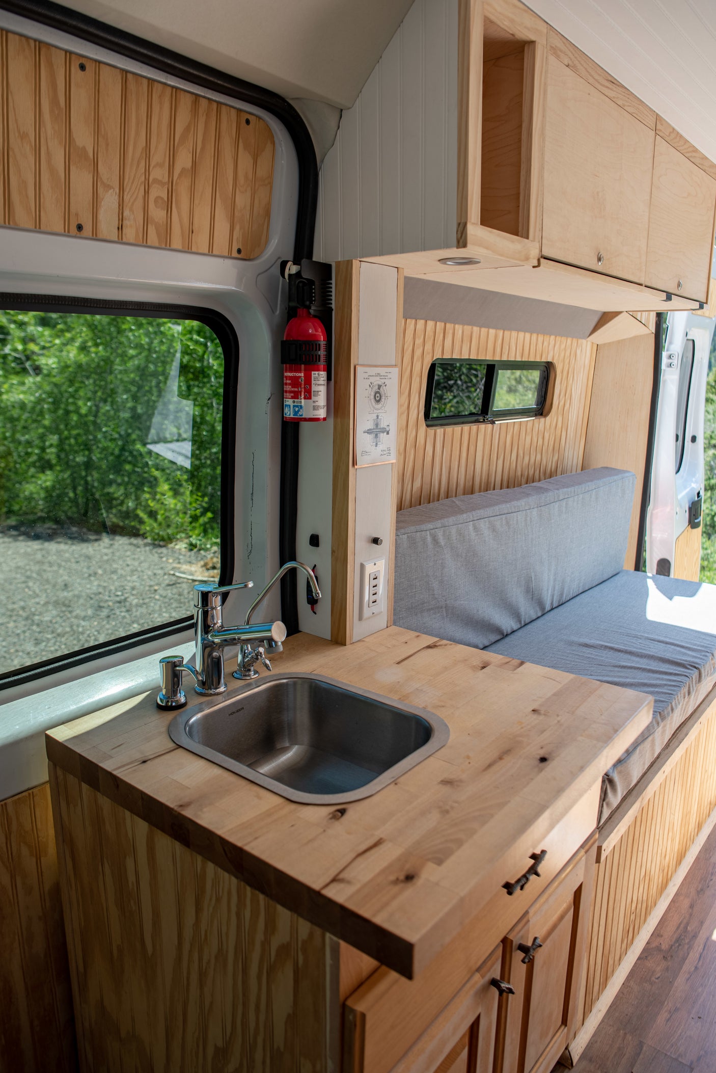Modern RV rental interior with kitchen sink, butcher block counter, and comfy bench seating/bed.