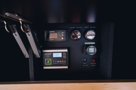 Check your RV rental's vital stats: control panel with fresh/grey water gauges, solar charge controller (12.2V), and heating controls.
