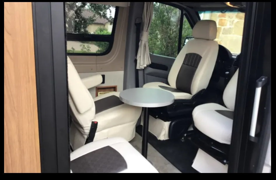 Inside an RV rental: swivel cream and brown captain's chairs surround a small table, creating a cozy living space for travel.