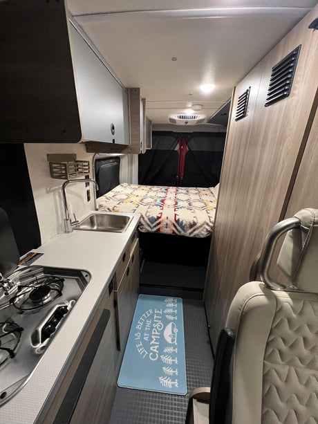 This RV rental's interior features a compact kitchen with sink/stove, comfy bed, and smart storage for road trips.